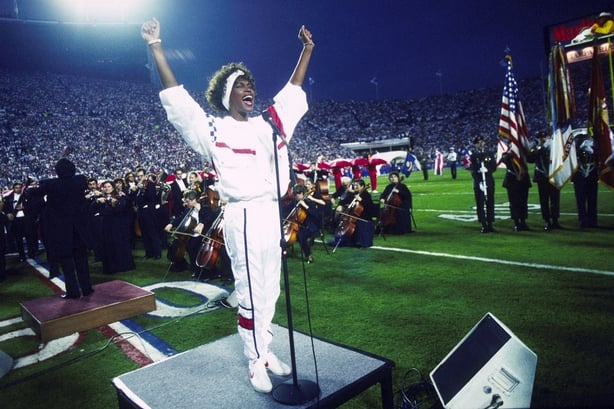 Whitney Houston sings the National Anthem during the pregame show at Super Bowl XXV while tens of thousands of football fans wave tiny American flags in an incredible outburst of patriotism during the Persian Gulf War on 01/27/1991. (Photo by Michael Zagaris/Getty Images)