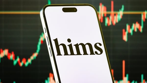 A smartphone displays the logo of Hims & Hers Health in front of a screen showing its latest stock market chart