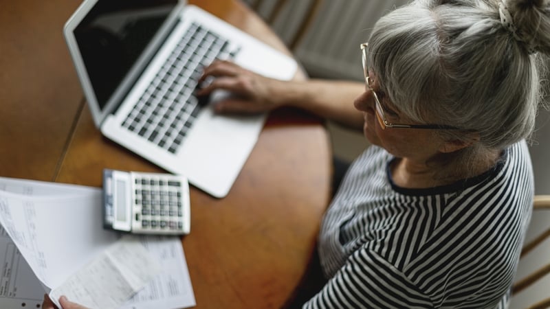 A woman with grey hair and glasses looking working with her laptop and calculator