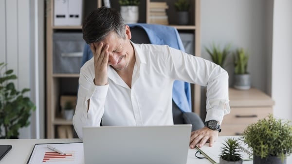 Stressed businessman experiencing a headache while working on a laptop in a modern office (Image: Getty Images)