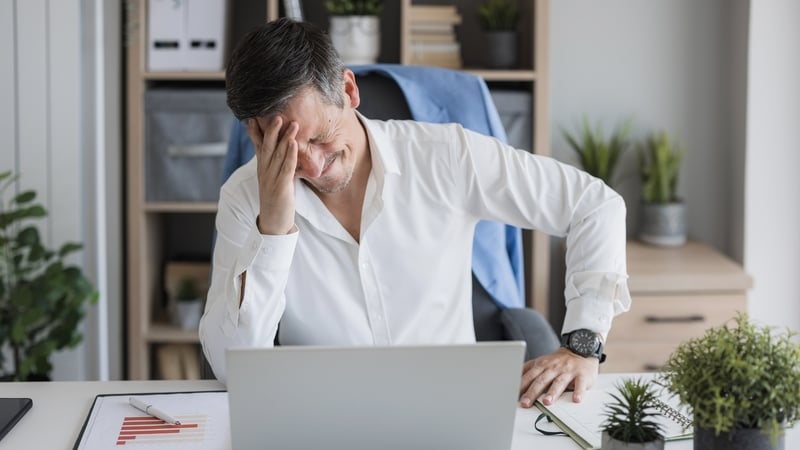 Stressed businessman experiencing a headache while working on a laptop in a modern office (Image: Getty Images)