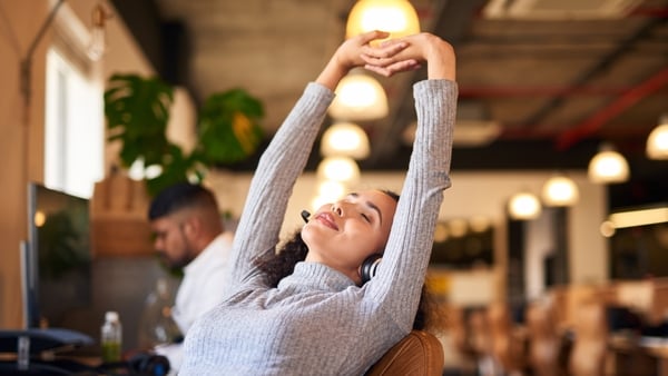 Young female call centre agent stretching at her desk in a modern office. Mixed race woman taking a break during work in call centre