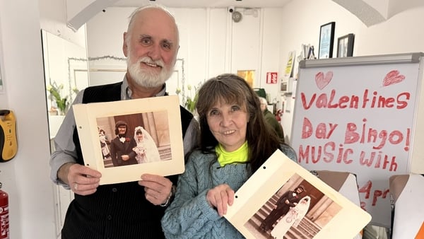 Paddy and Maura O’Brien stand together holding their wedding photos towards the camera