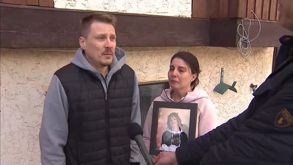 A man and woman, both crying, hold a photograph of a child