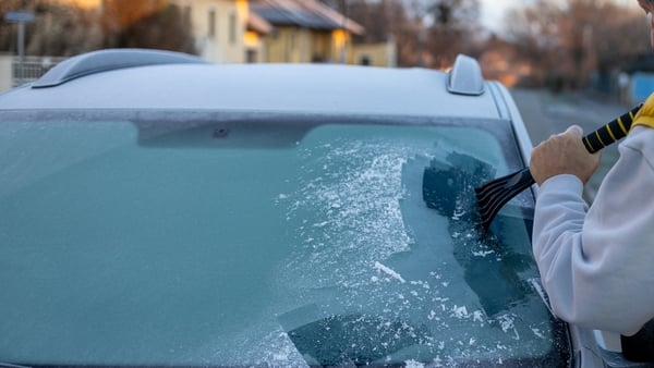 Elderly man cleans windshield with ice scraper