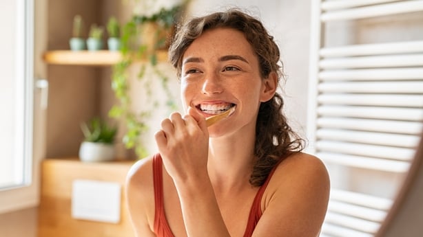 Smiling young woman brushing teeth in bathroom.