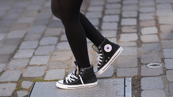 A person wears black tights and black canvas high-top Converse runners with white laces