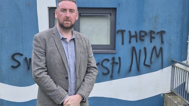 A man stands in front of a building with graffiti written on it