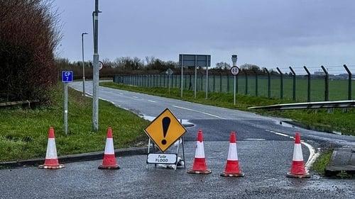 A weather radar dish is shown mounted on a building at Dublin Airport, with a backdrop of the airport's runway and terminal buildings.