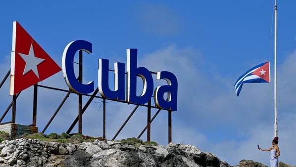 A tourist takes a selfie picture as she stands next to a Cuban national flag at half-mast in Havana on January 5, 2026. Havana declared two days of national mourning as of January 5 after a total of 32 Cubans were killed during the US attack on Caracas th