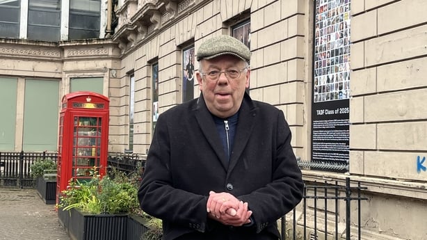a photograph of a man called john gray with a red telephone box in the background