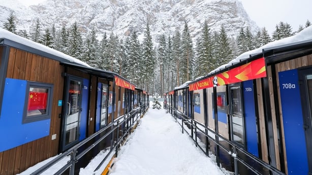 A line of cabins with a snowy mountain and trees in the background