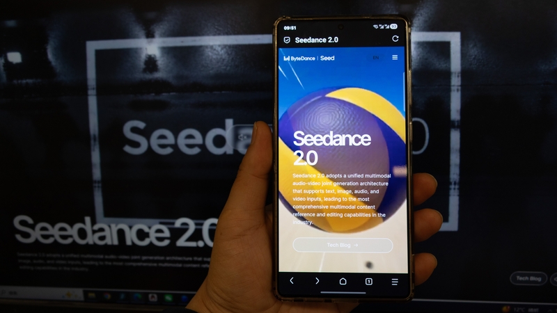 A person holds a mobile phone with Seedance2.0 on it with a computer screen in the background