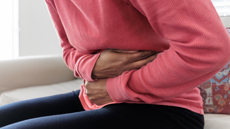 Close-up of unrecognizable black woman sitting on couch holding her abdomen in pain