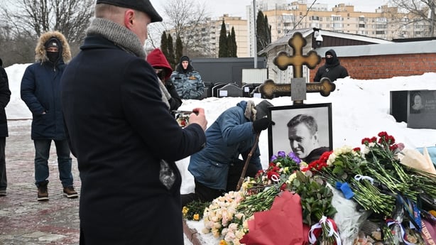 A man visits the grave of Russian opposition leader Alexei Navalny, which has multiple floral tributes