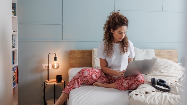 woman working from home and sitting in bed on laptop