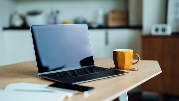 Laptop computer with blank screen, smartphone, notebook and a cup of tea on wooden table in the living room at home by the window against beautiful sunlight