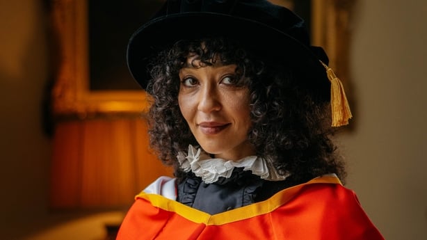 A head and shoulders image of actress Ruth Negga smiling at the camera while wearing red and white robes.