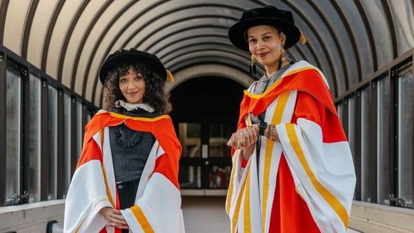Two women wearing red and white robes smile at the camera.