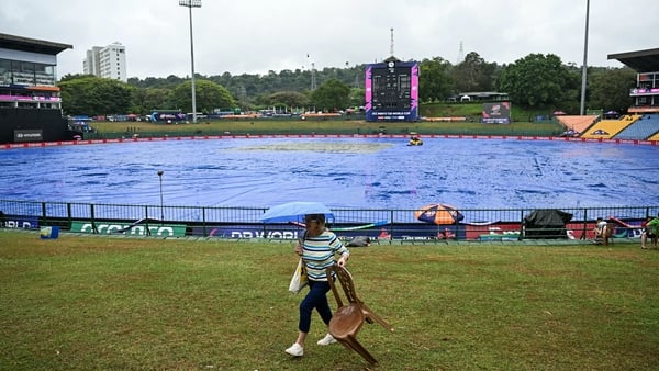 A cricket fan carrying an umbrella walks past the covered pitch as rain delays the start of the 2026 ICC Men's T20 Cricket World Cup group stage match between Zimbabwe and Ireland at Pallekele International Cricket Stadium in Kandy on February 17, 2026. (