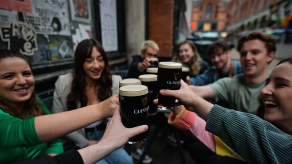 People drinking Guinness outside a pub, bringing glasses together to say cheers