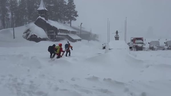 Three people in snow gear walk through deep snow