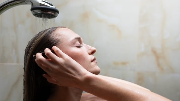 Woman washing her hair under a shower, eyes closed in a moment of self care and relaxation