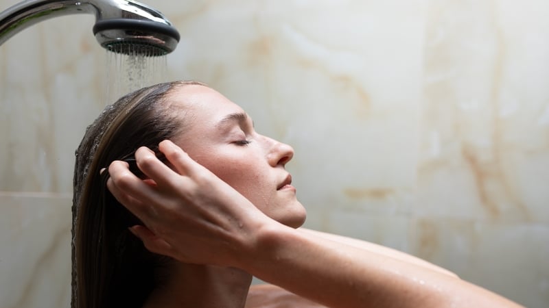 Woman washing her hair under a shower, eyes closed in a moment of self care and relaxation