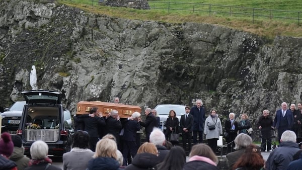 Pall bearers carry a coffin as crowds of people look on
