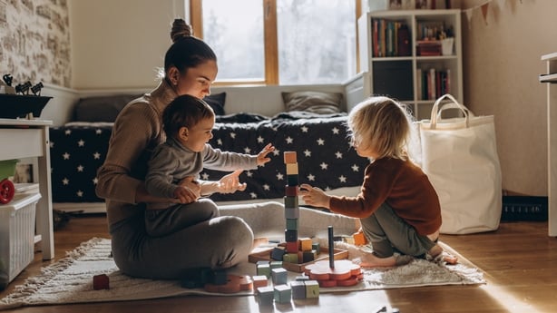 Young Mother playing with children while sitting on floor at home with wooden toys