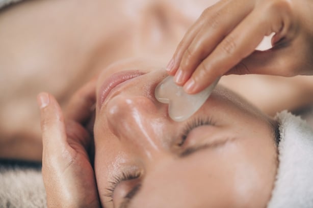 Young woman receiving a guasha face sculpting massage with a jade stone.
