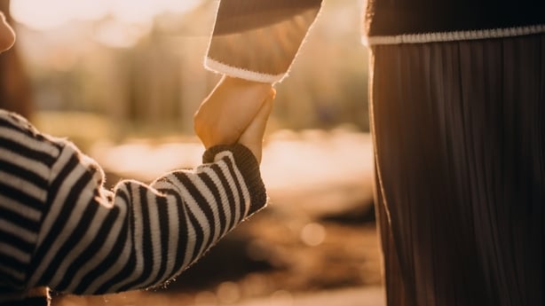 Close-up of young Asian mother walking hand in hand with her daughter enjoying family bonding time in park at beautiful gold-coloured sunset. Healthy family lifestyle. Family love, bonding and togetherness