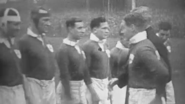 A black and white still of rugby players shaking hands