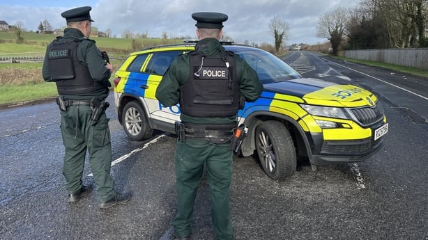 Two PSNI officers with their backs to the camera stand in front of a police car
