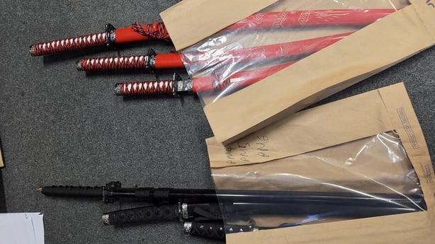 a number of machete type weapons in red and black displayed on garda evidence bags