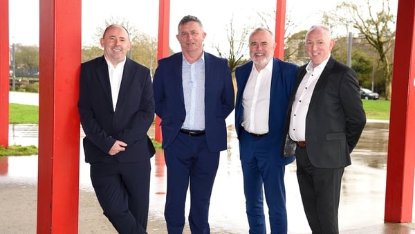 Four business men pose for a photo with red pillars in the background