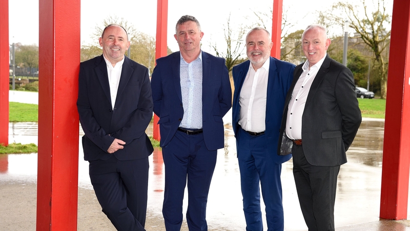 Four business men pose for a photo with red pillars in the background