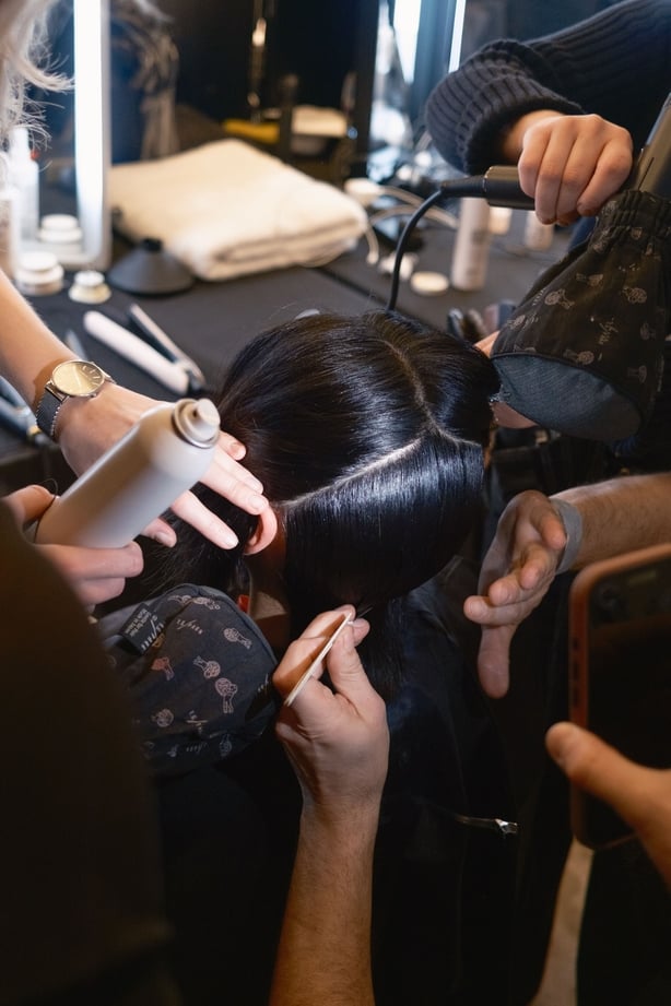 A number of hairdressers working on a model's hair back stage