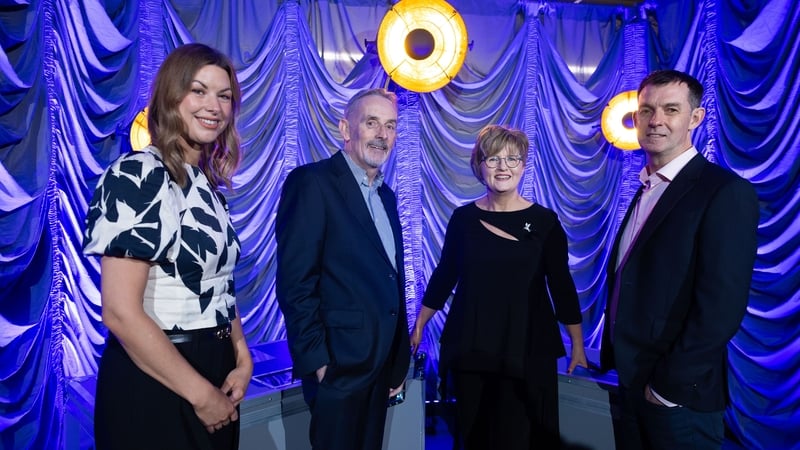 Business men and women pose for a photo with an events stage behind them