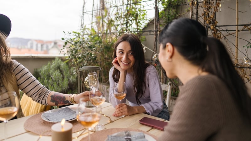 Photo of a diverse group of people snacking, drinking and enjoying an outdoors dinner party, on a balcony of an apartment