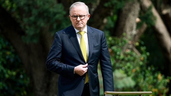 Australia's Prime Minister Anthony Albanese in a suit and tie walking towards the camera with trees behind