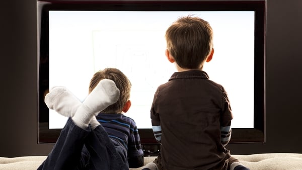 Two half Asian Brothers sitting and laying down on a day bed in front of a large flat screen TV on location
