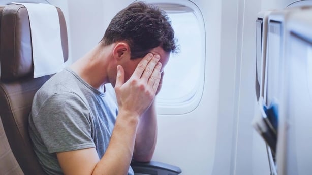 A man rubbing his temples while on a flight