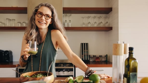 Healthy senior woman smiling while holding some green juice in her kitchen.