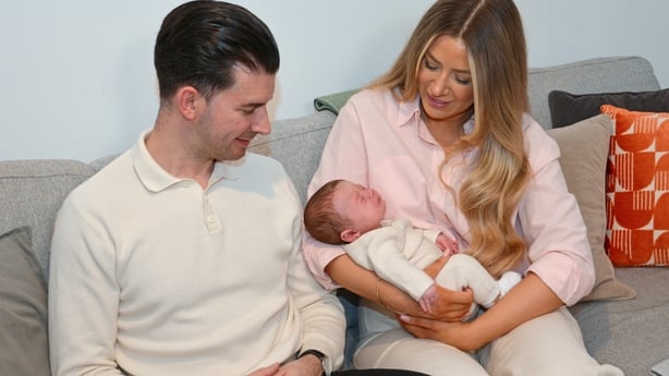 a man and a woman look down at a small baby being held by the woman