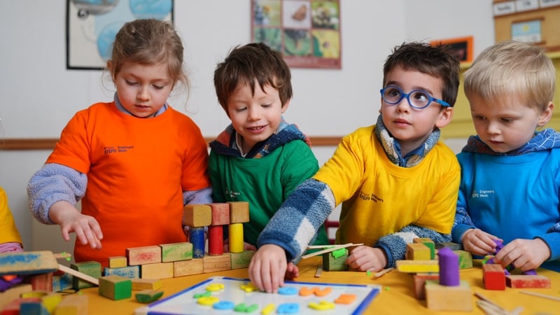 4 Children play with building bricks at a table in a classroom