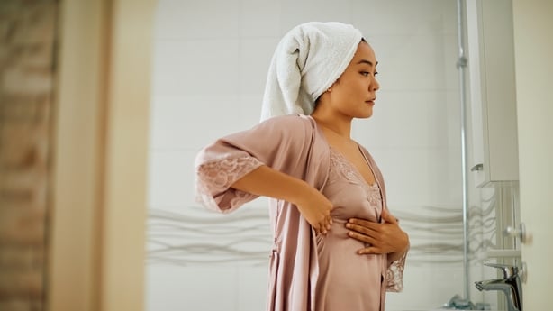 Young Asian woman standing in front of bathroom mirror while doing breast self-examination. 