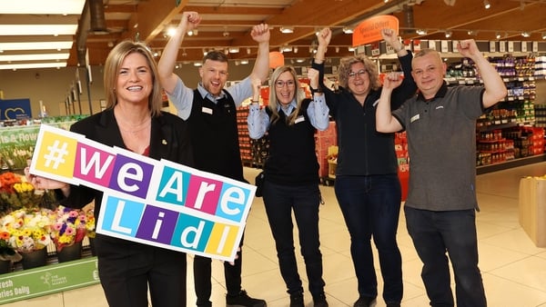 Lidl employees in the supermarket aisle look happy with their arms punching the air as they celebrate a pay increase
