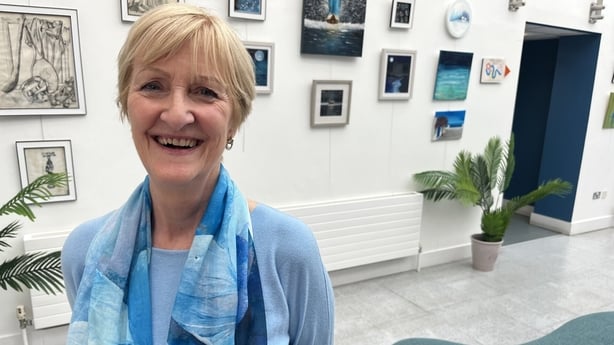 Sheila McAdam stands in front of framed artwork.