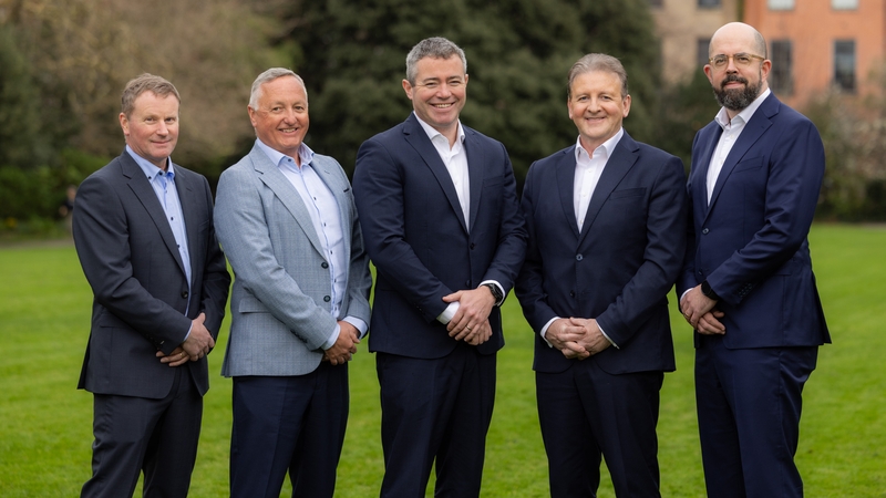 Five businessmen in suits pose for a photo in a garden